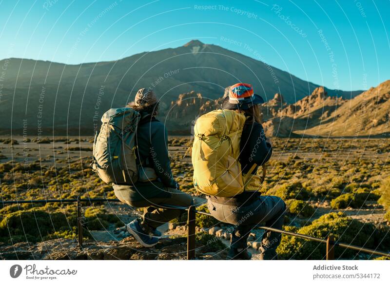 Anonymous hikers resting during trekking in highlands couple traveler mountain fence trip tourist nature friend adventure backpack tenerife spain blue sky