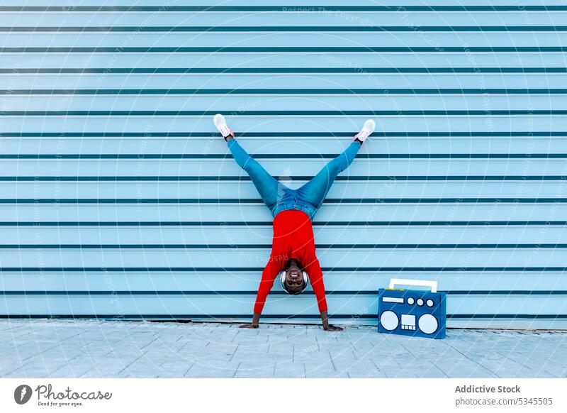 Optimistic young woman standing on arms on street handstand headphones listen music boombox split smile optimist female black african american funky song