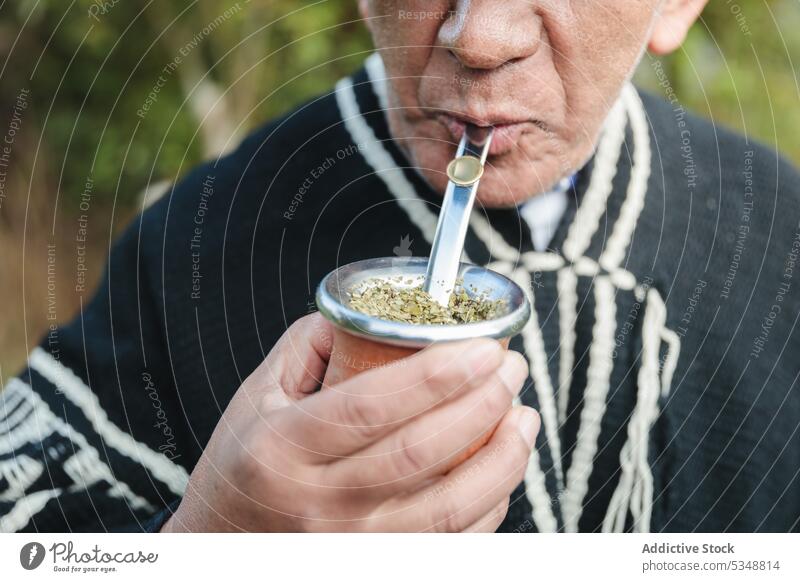 Cropped senior man drinking hot beverage in park yerba mate straw knitted mapuche indigenous temuco chile chilean traditional woolen rural elderly male aged