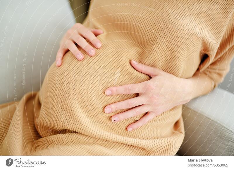 Pregnant caucasian woman resting at home. A young expectant mother reads a  doctor's report and looks at ultrasound pictures of her baby. Expectant mom  strokes her pregnant belly and thinks about baby 