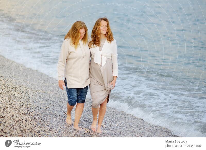 Redhead senior mother and her adult beautiful pregnant daughter are walking together on the sea shore. people maternity family look alike talk parent hang out