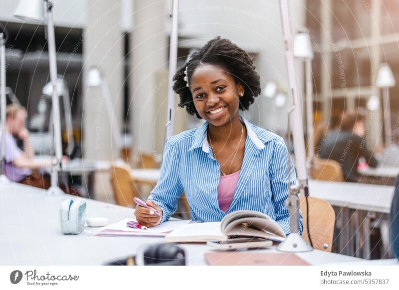 Young black woman writing in notebook in a library real people teenager campus positive exam knowledge confident academic adult lifestyle academy adolescent