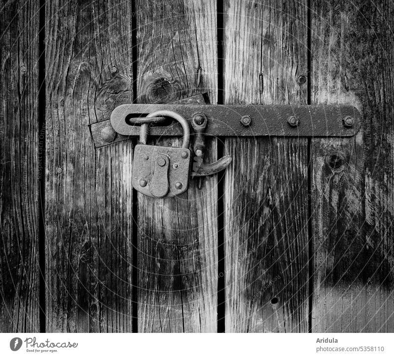 Old padlock locks a barn door made of weathered boards Padlock Lock locked completed Flake Barn Goal Wood Washed out Weathered Closed Safety Entrance Metal