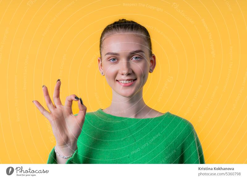 Pretty woman with OKAY sign, ok gesture. Happy lady, correct choice on yellow good okay yes agreement hand satisfaction symbol approve leisure lifestyle model