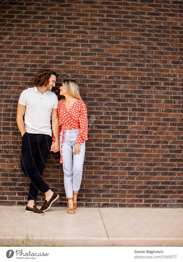 Smiling young couple in love in front of house brick wall adult beautiful casual caucasian cheerful cute facade female happiness happy home lifestyle man new