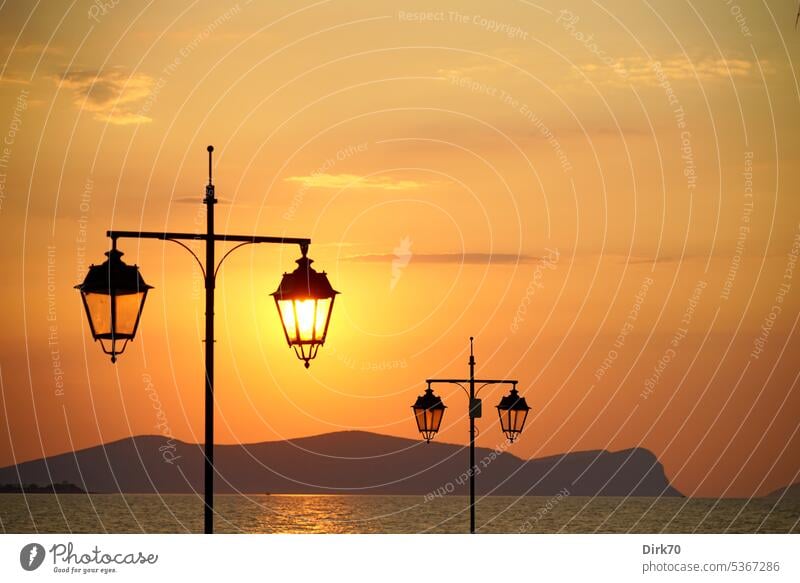 Rising sun behind street lamp with view of sea with islands in background Ocean Mediterranean sea Saronic Gulf the Aegean Aegean Sea Lantern streetlamp