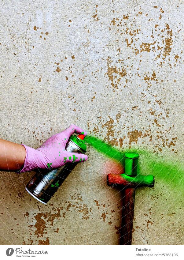 Art project! An old film can is sprayed with green paint. The hand holding a spray can is protected with a disposable pink glove. Wall (building) Concrete