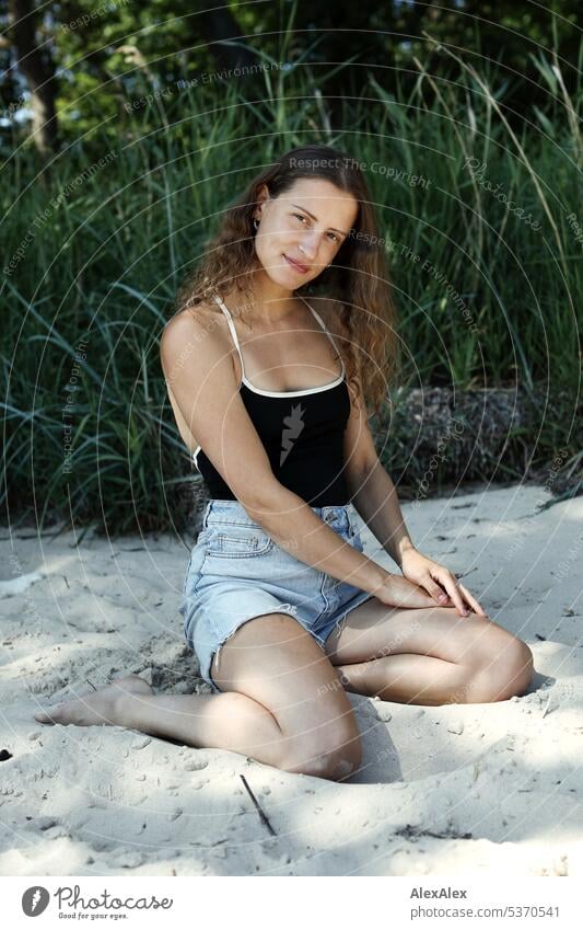 side portrait of young beautiful brunette smiling woman kneeling in the sand in front of a forest warm Summery Beautiful weather plants proximity Day