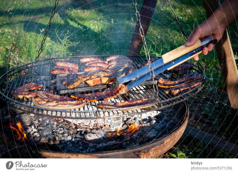 Grilling meat and sausages over an open fire BBQ Fire Meat BBQ season fire bowl Nutrition Embers Smoke Summer Delicious Hot Turn meat barbecue tongs Garden