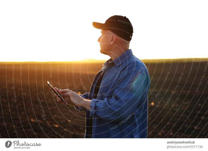 Smart farming technology and agriculture. Farmer uses digital tablet on field with plowed soil at sunset. Checking and control of soil quality, land readiness for sowing crops and planting vegetables