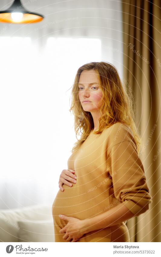 Pregnant caucasian woman relaxing at home. Young expectant mother strokes  her pregnant belly and thinks about the baby childbirth. - a Royalty Free  Stock Photo from Photocase