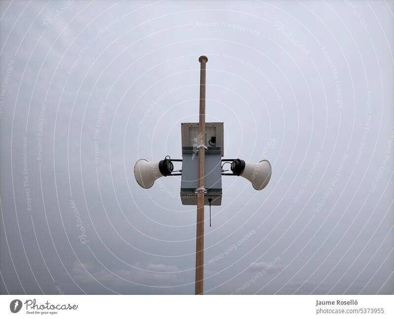 Two white speakers on a mast outdoors advertisement audio communicate control festival information loud religious volume promotion voice cartoon business speech