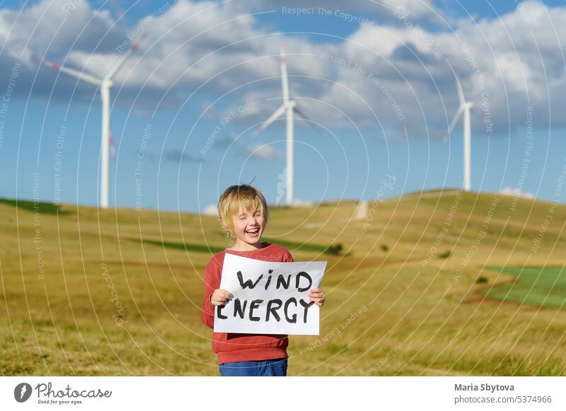Eco activist boy with banner "Wind Energy" on background of power stations for renewable electric energy production. Child and windmills. Wind turbines for generation electricity. Green energy