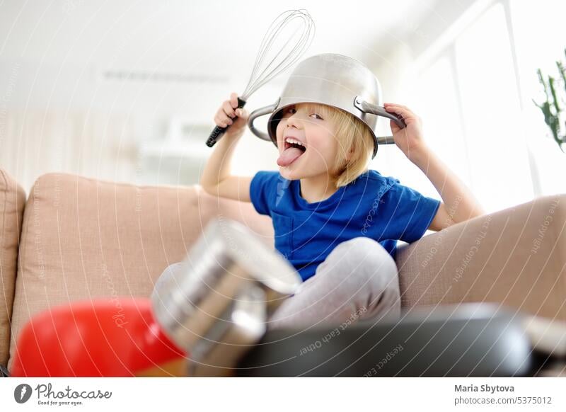 Mischievous preschooler boy play the music using kitchen tools and utensils at home during quarantine. Funny drum part from child. Entertainment a kids at home.