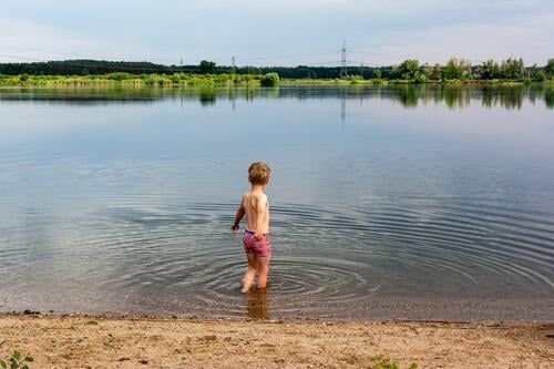 Boy stands in the water of a gravel lake and hesitates a little before bathing gravel pit Swimming lake Bathing place Boy (child) Rear view Lake Water Summer