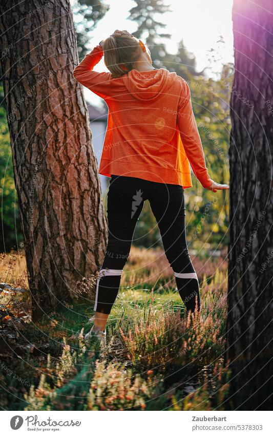 Woman jogging in back view doing stretching exercise between two trees Jogging Sports Walking Distend Warming up Forest Nature Orange Back-light Fitness