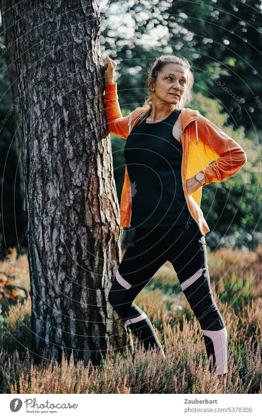 Woman jogging in forest doing stretching exercise on tree Jogging Sports Walking Distend Warming up Forest Nature Orange Back-light Fitness Athletic Healthy