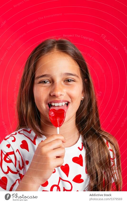 Cute little girl licking red lollipop portrait candy sweet positive smile happy kid adorable cute casual child childhood long hair tasty style delight