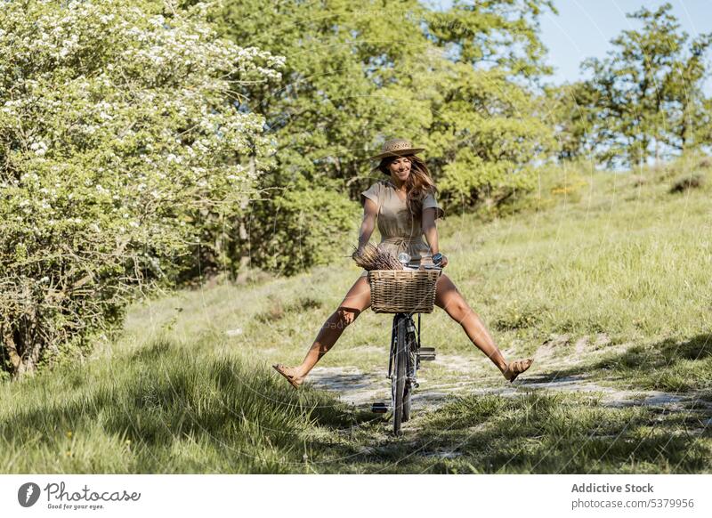 Cheerful woman riding bicycle in countryside ride legs up nature summertime having fun joy cheerful carefree happy female young straw hat overall style rural