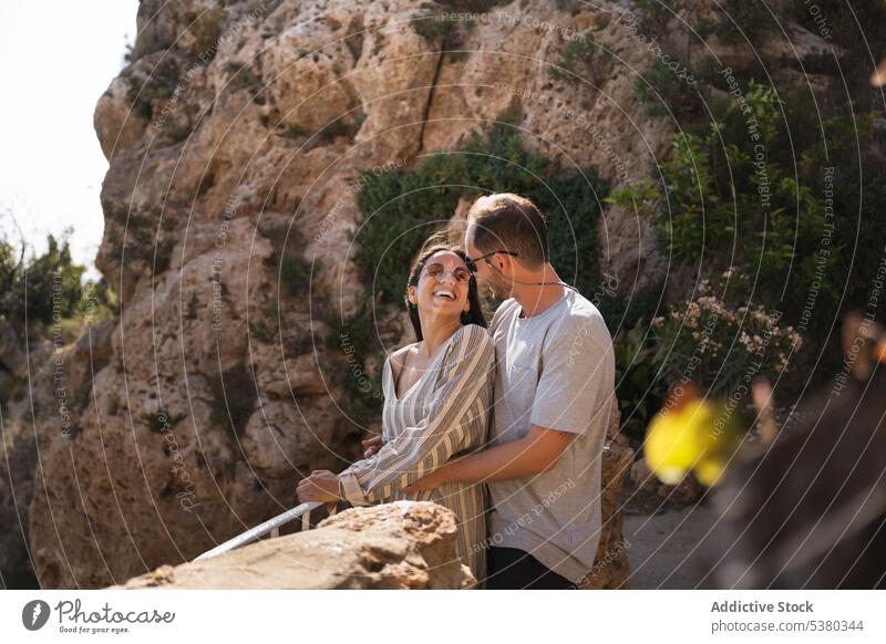 Happy couple standing close together on rocky cliff relationship mountain cuddle vacation smile bonding fondness affection romantic adventure embrace young