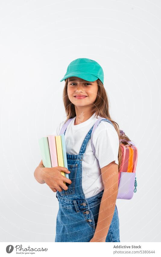 Cheerful schoolgirl with backpack smile positive student kid education happy notebook pupil child denim hat carry little glad studio shot knowledge childhood