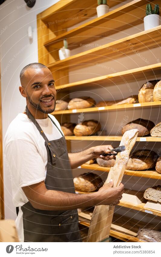 Happy black man putting bread in paper bag bakery seller grocery shop small business work baked owner food staff male pastry positive job store purchase smile