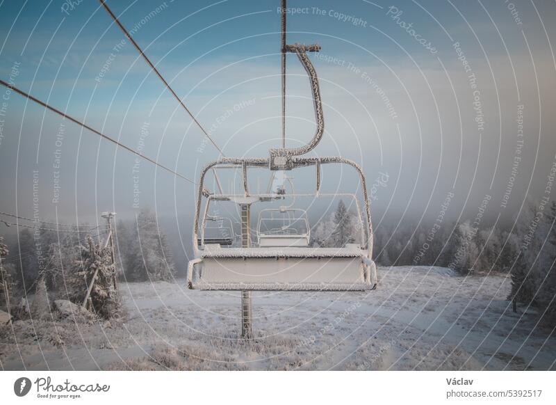 Sunrise breaking through the thick white fog at the top of Vuokatti Hill, a ski resort in Vuokatti, Finland. A view of the frozen chairlift. The Scandinavian experience of winter