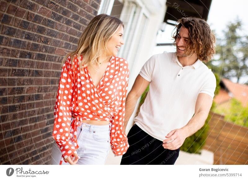 Smiling young couple in love walking in front of house brick wall adult beautiful casual caucasian cheerful cute facade female happiness happy home lifestyle