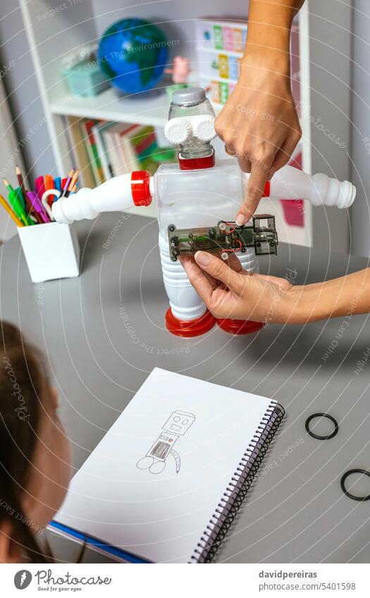 Teacher explaining how to connect electric circuit on recycled toy robot unrecognizable teacher female child robotic electronic electrical technological