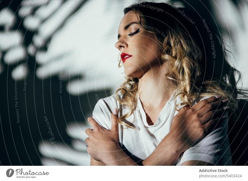 Young woman with red lips standing near wall sensual eyes closed shadow reflection posture female young shirt allure style sunlight feminine sensitive calm