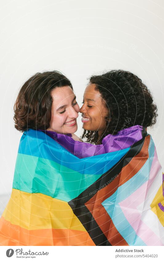 Happy diverse young friends with LGBT flag lesbian couple lgbt relationship love eyes closed hug smile embrace female multiethnic multiracial homosexual women
