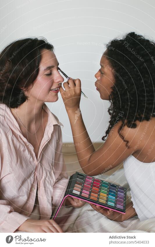 Black woman applying makeup with brush on eye of girlfriend women at home eyeshadow smile beauty positive young female diverse multiracial multiethnic cosmetic