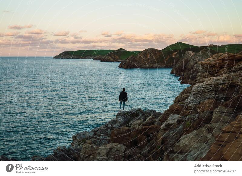 Anonymous traveler standing on rocky cliff near ocean sea tourist spectacular scenery nature breathtaking leisure wanderlust sunset admire cantabria sky
