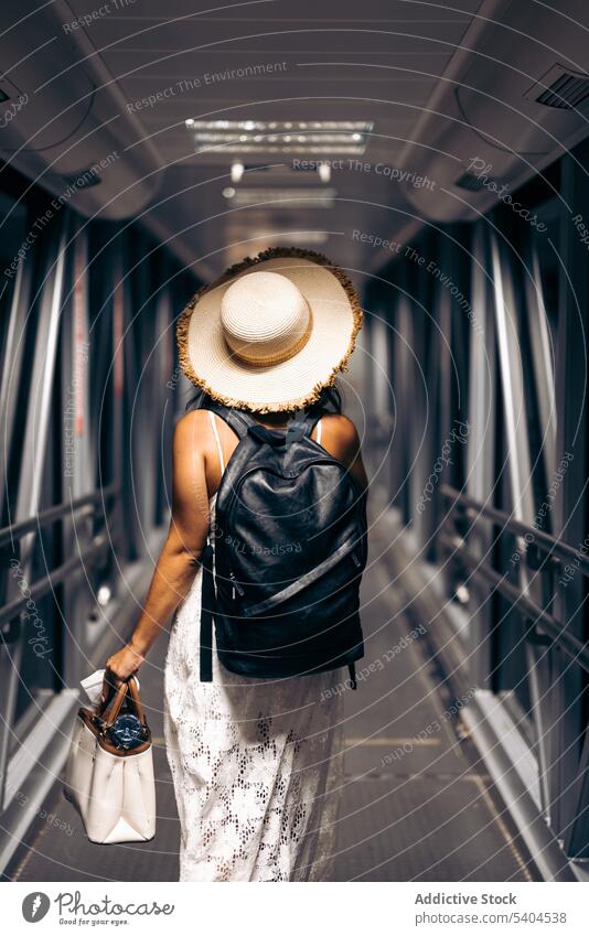 Anonymous woman with backpack in boarding bridge passenger tourist journey corridor vacation flight trip travel female tourism destination traveler walk hat