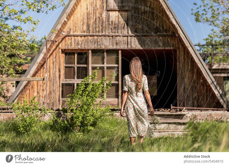 Anonymous woman walking to house in countryside summer shed barn village rural nature dress wooden bright land freedom building alone structure green