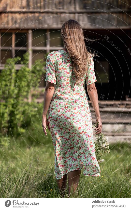 Anonymous woman walking to house in countryside summer shed barn village rural nature dress wooden bright land freedom building alone structure green