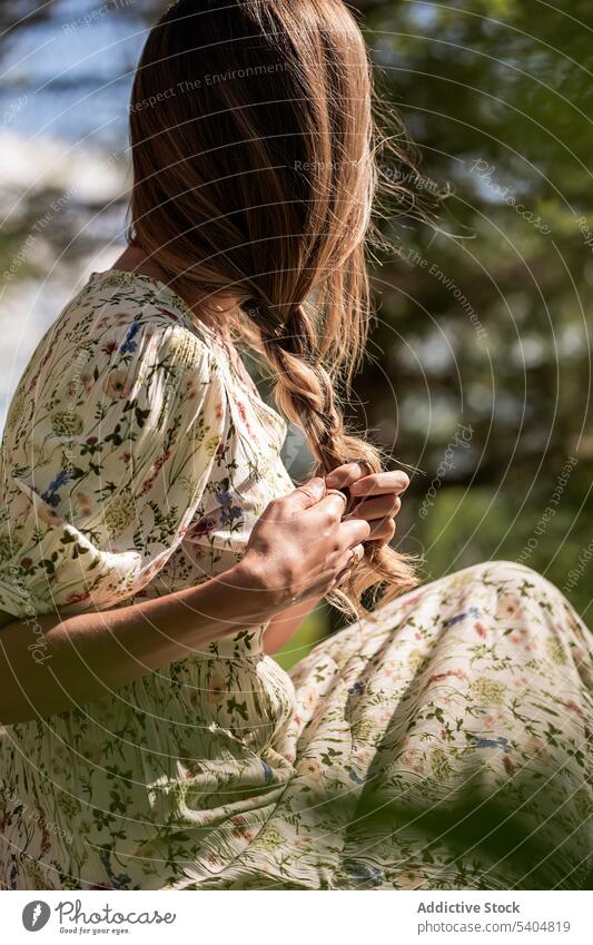 Unrecognizable woman braiding hair in nature meadow hairstyle countryside dress long hair peaceful tranquil serene summer rest rural flora harmony female floral