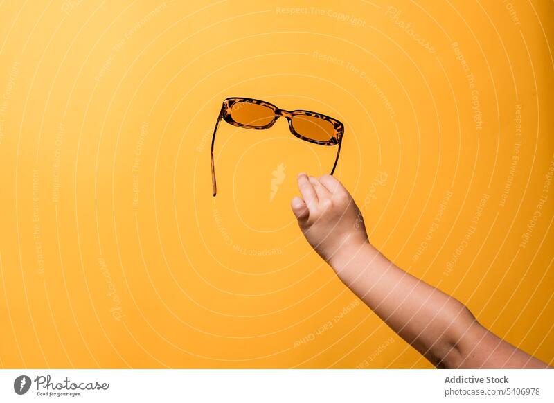 Crop anonymous kid showing sunglasses in yellow studio child demonstrate accessory style hand girl fashion bright arm arm raised childhood design trendy holiday