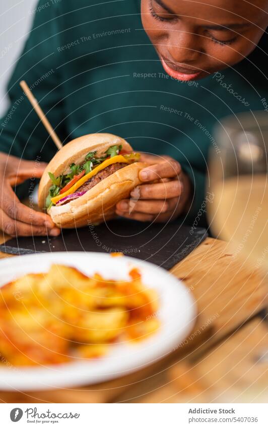 African American woman eating delicious burger tasty snack restaurant cafeteria portion food young hungry dish plate yummy table meal hamburger lunch female