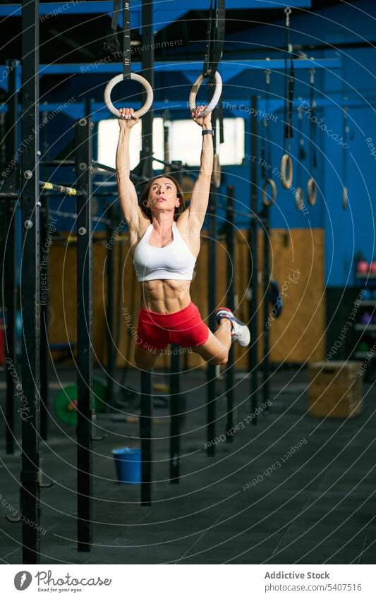 Strong female athlete pulling up on gym rings sportswoman exercise hang training muscular challenge stamina workout adult fitness physical healthy lifestyle