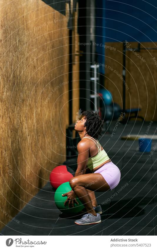 Strong black sportswoman throwing medicine ball against wall exercise power weight training gym crouch mature african american ethnic afro equipment muscular