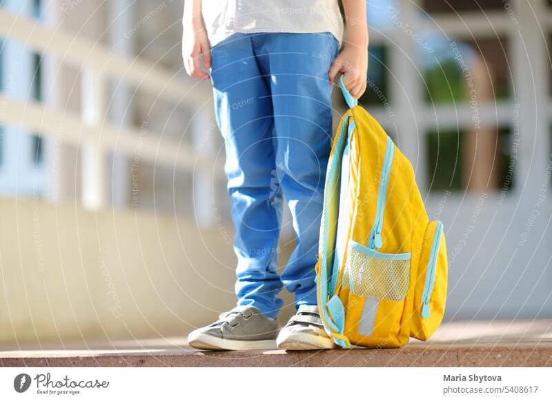 Little student with a backpack on the steps of the stairs of school building. Close-up of child legs, hands and schoolbag of boy standing on staircase of schoolhouse.Back to school concept.