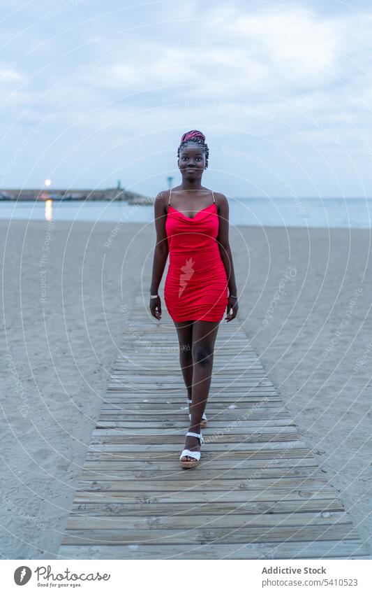 Happy African American woman walking on pier ocean style sea confident sky serious dress fashion trendy lady nature red alone modern slim lifestyle seaside