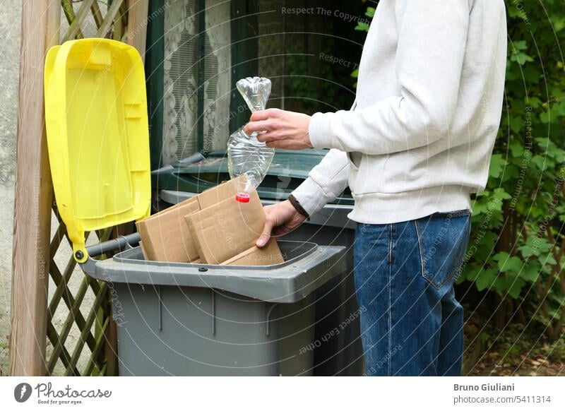 A man sorting waste. A person throwing cardboard packaging and a plastic bottle into a yellow recycling bin. ecology environmental garbage garbage bin green