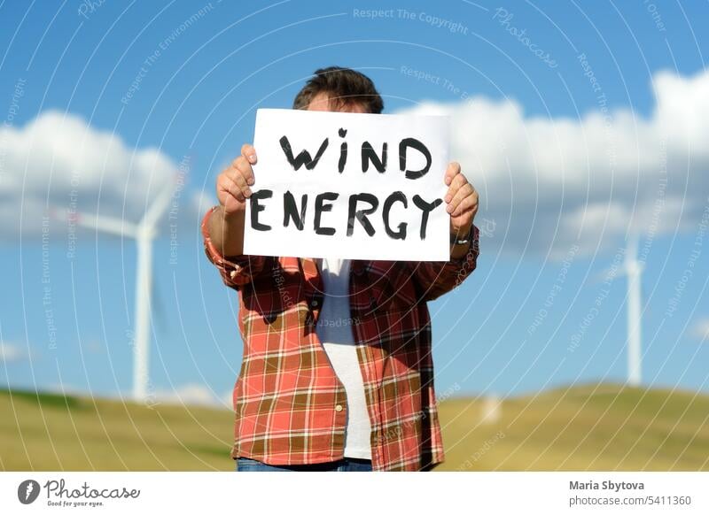 Eco activist with banner "Wind Energy" on background of power stations for renewable electric energy production. Person and windmills. Wind turbines for generation electricity. Green