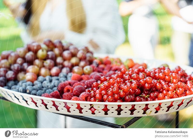A dish with a variety of summer berries, red currants, raspberries, blueberries, gooseberries, grapes during an outdoor event in summer fresh strawberries