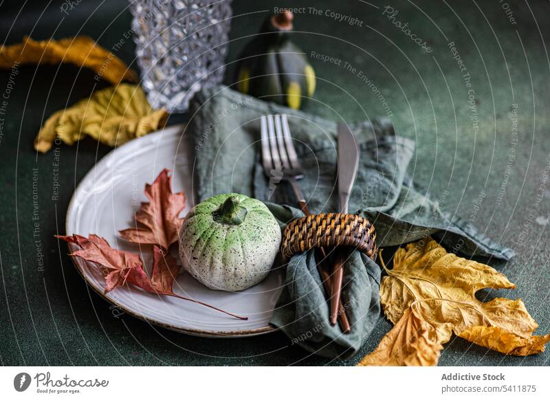 Autumnal table setting against dark background autumnal cutlery fork knife napkin plate tablecloth tableware leaf colorful small pumpkin empty glass transparent