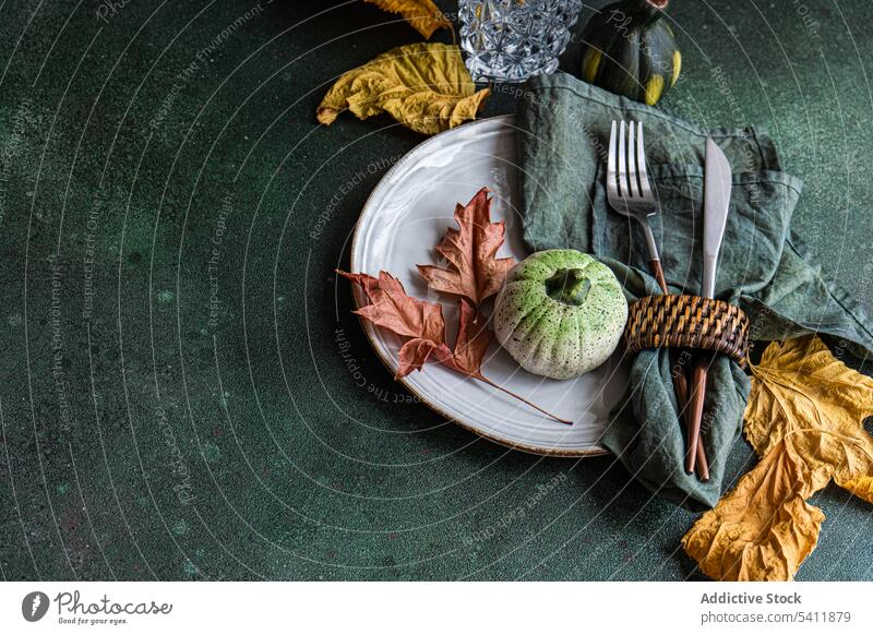 Autumnal table setting against dark background autumnal cutlery fork knife napkin plate tablecloth tableware leaf colorful small pumpkin empty glass transparent