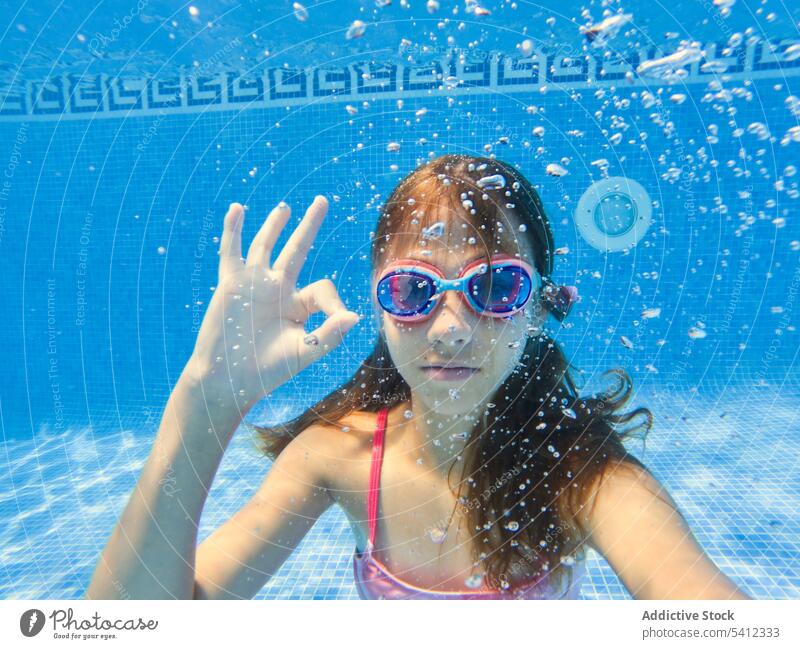 Positive girl in eyeglasses gesturing OK inside swimming pool water ok finger sign gesture swimwear portrait confident vacation calm relax smile peace swimsuit