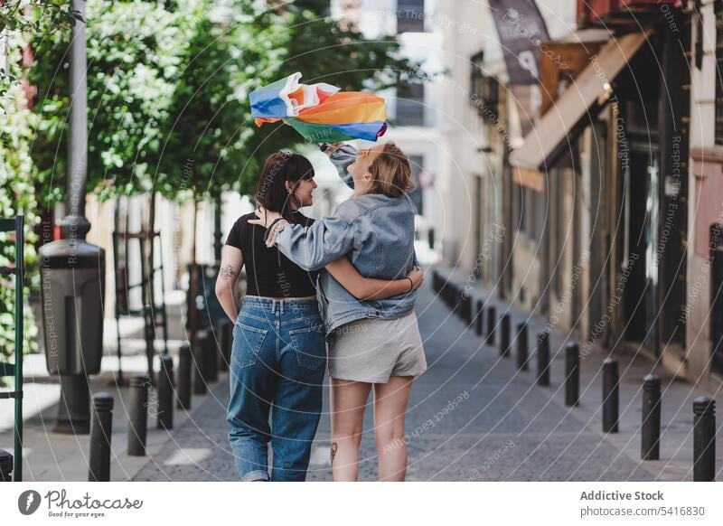 Lesbian couple with LGBT flag walking on street lesbian lgbt hugging happy waving city young together women casual homosexual pride equality alternative